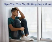 Teen boy sitting in window ledge with hand in his hair, having anxiety.