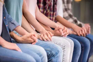 White teens in a group therapy session holding hands.