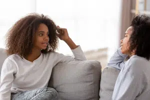 Mom and teen daughter on couch talking through a family conflict.